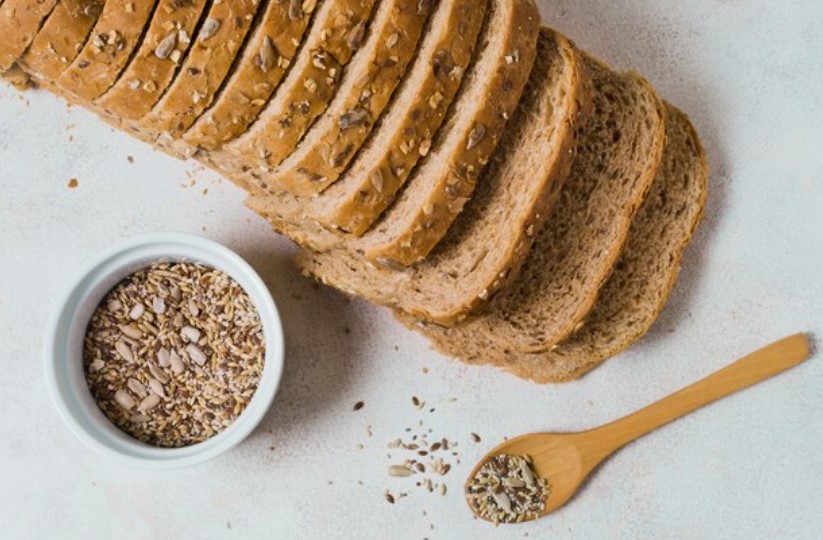 A bowl of freshly made gluten free bread crumbs on a kitchen counter, surrounded by gluten free bread and herbs